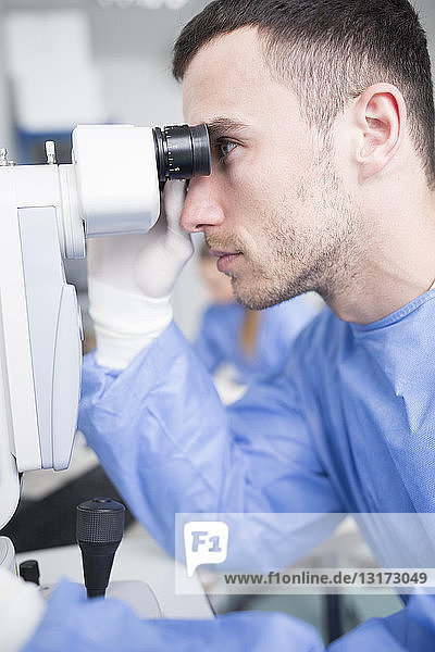 Laborant  der durch ein Mikroskop schaut