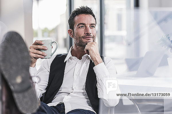 Businessman sitting in office  drinking coffee  with feet up
