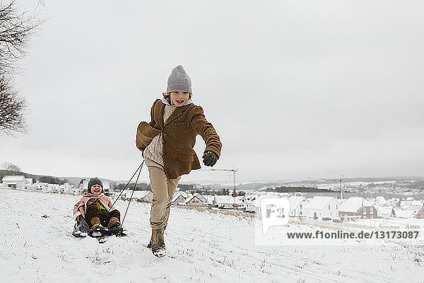 Boy pulling sledge with little sister in snow