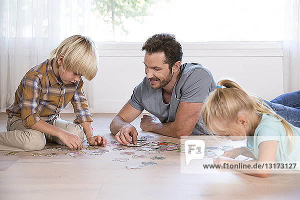 Vater mit zwei Kindern  die zu Hause auf dem Boden liegen und Puzzle spielen