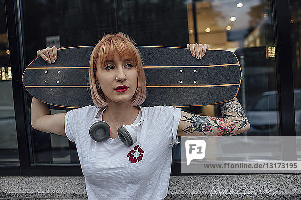 Junge Frau hält Carver-Skateboard vor einem Gebäude