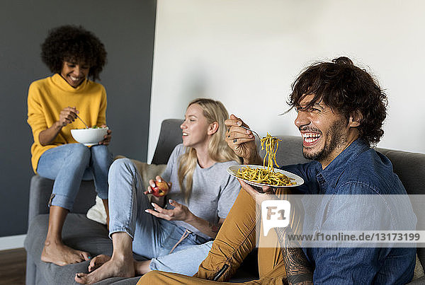 Cheerful friends sitting on couch talking and eating