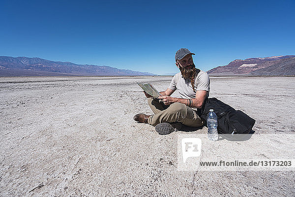 USA  Kalifornien  Death Valley  Mann sitzt in der Wüste mit Karte auf dem Boden und ruht sich aus