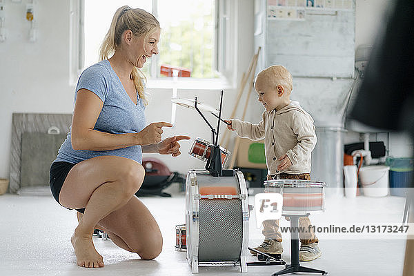 Glückliche schwangere Mutter mit Kleinkind spielt Spielzeugtrommeln