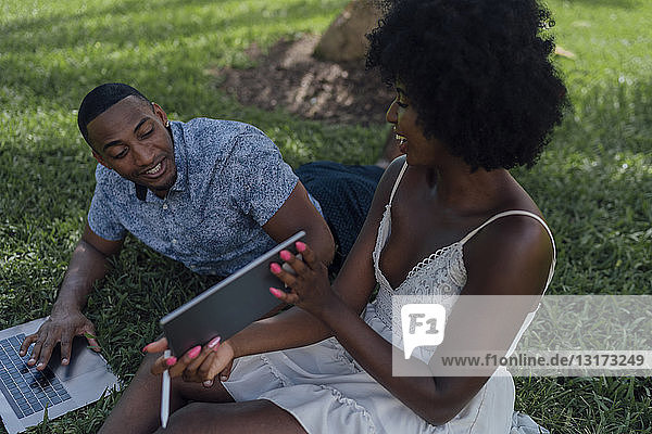 Glückliche junge Frau zeigt ihrem Freund eine Tablette auf einem Rasen in einem Park