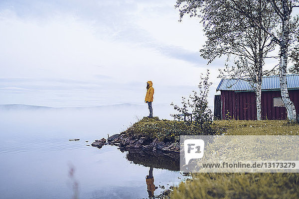 Schweden  Lappland  Mann mit Windjacke steht am Wasser und schaut in die Ferne