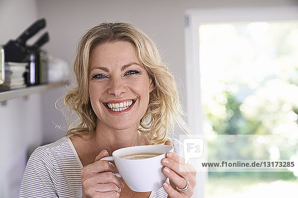 Porträt einer lächelnden Frau  die in der Küche Kaffee trinkt
