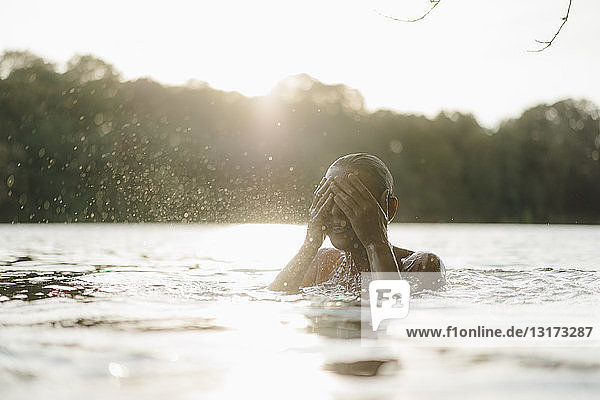 Frau in einem See bei Sonnenuntergang  die mit Wasser spritzt