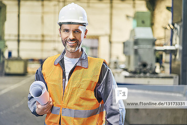 Porträt eines lächelnden Mannes mit Blaupausen in der Fabrik