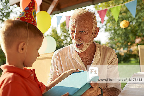 Grossvater übergibt Geschenk an Enkel auf einer Gartengeburtstagsfeier