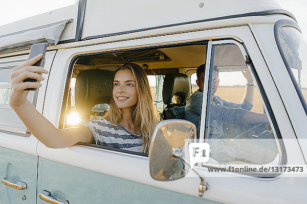 Smiling woman taking a selfie in a camper van with man driving