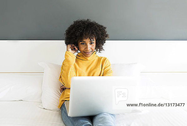 Lächelnde Frau sitzt mit Laptop auf dem Bett