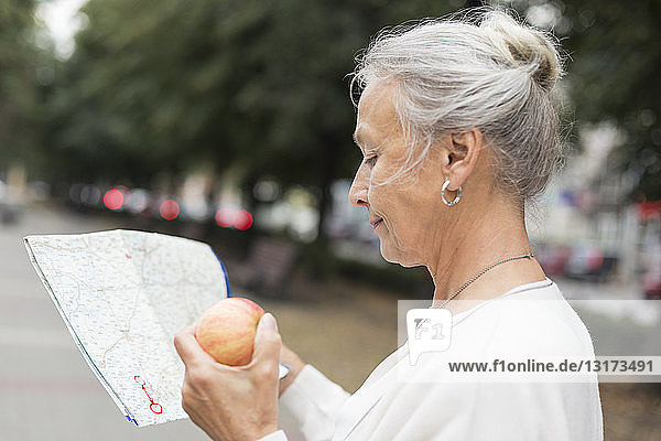 Ältere Frau im Freien mit Karte und Apfel in der Hand