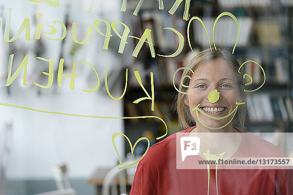 Porträt einer glücklichen jungen Frau hinter einer Fensterscheibe in einem Cafe