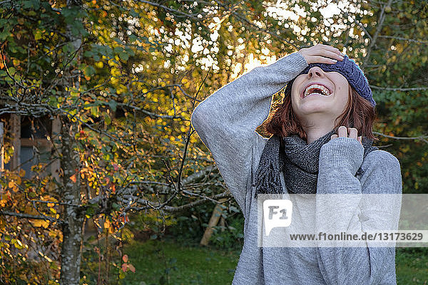 Lachendes Teenagermädchen mit Wollmütze und Schal im Herbst