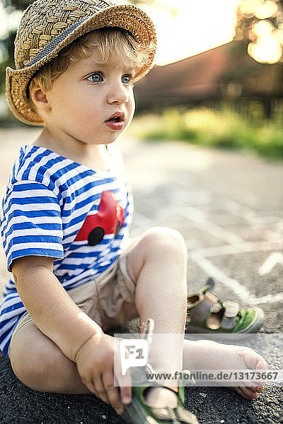 Portrait of toddler boy sitting on the street taking off his shoes