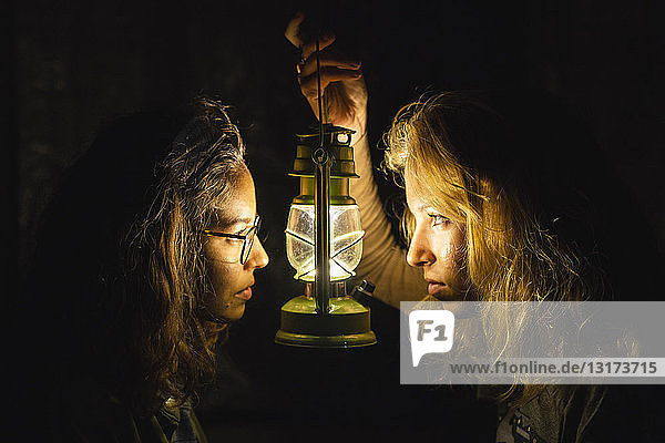 Two young women with storm lantern in the dark facing each other