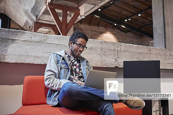 Junger Mann  der in einem kreativen Start-up-Unternehmen arbeitet und einen Laptop benutzt