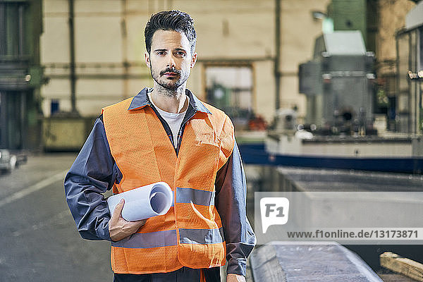 Portrait of serious man holding blueprints in factory