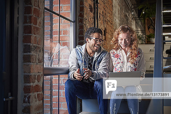 Young business people sitting on stairs in loft office using laptop