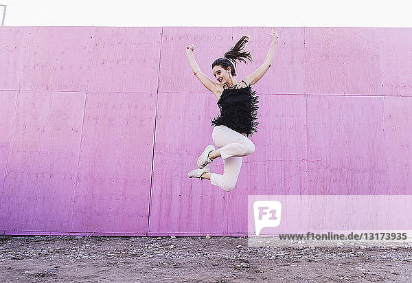 Überschwängliche junge Frau springt vor rosa Wand