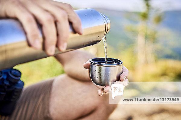 Close-up of man during hiking trip pouring cold water from thermos flask