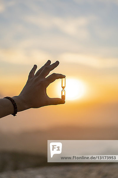 Close-up of man's hand holding an hourglass at sunset