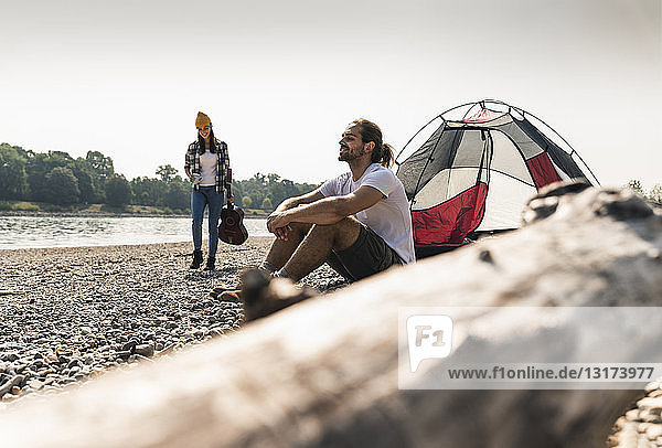 Junges Paar entspannt sich am Flussufer mit Gitarre und Zelt
