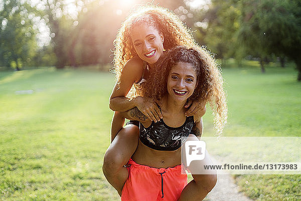 Portrait of smiling young woman giving her twin sister a piggyback ride