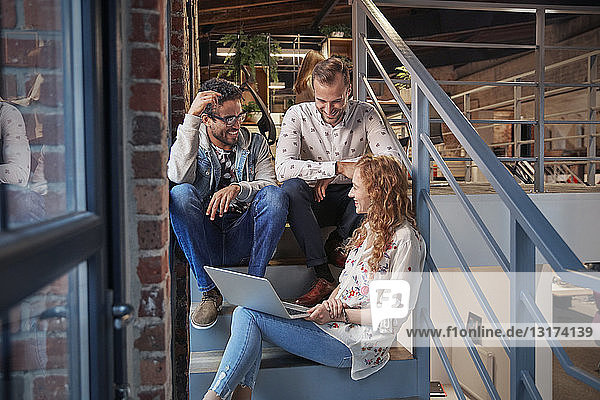Young business people sitting on stairs in loft office using laptop