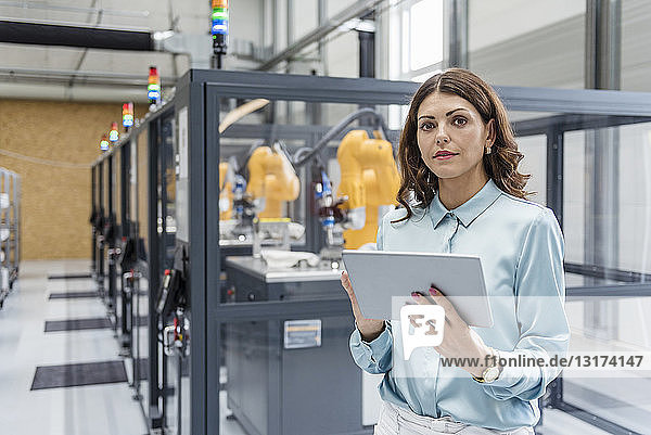 Geschäftsfrau in einem High-Tech-Unternehmen  die Industrieroboter mit Hilfe eines digitalen Tablets steuert
