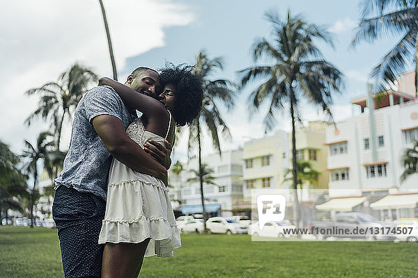 USA  Florida  Miami Beach  glückliches junges Paar  das sich im Sommer in einem Park umarmt