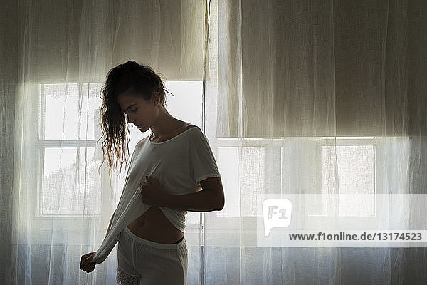Young woman standing in front of window in white underwear