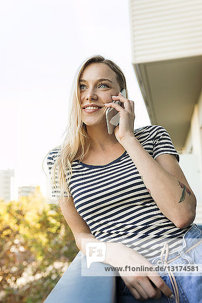 Smiling young woman talking on cell phone on balcony