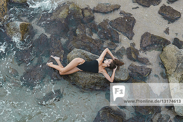 Draufsicht auf eine schöne junge Frau  die auf einem Felsen im Meer liegt