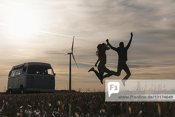 Überschwängliches Paar springt in der Abenddämmerung auf Wohnmobil in ländlicher Landschaft