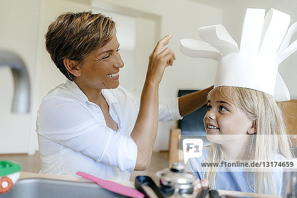 Happy mother and daughter playing at home putting on chef's hat