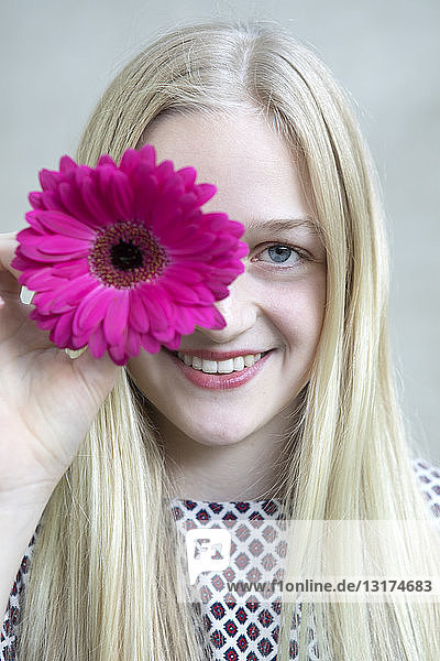 Bildnis eines lächelnden blonden Mädchens mit Blumenkopf aus rosa Gerbera