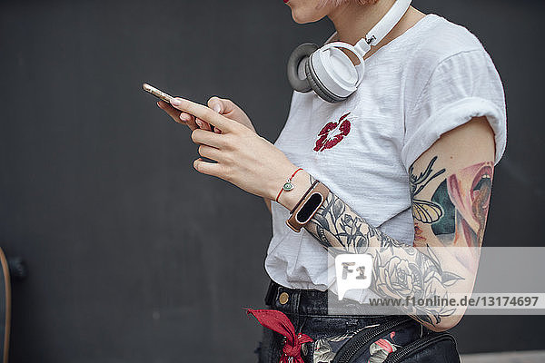 Nahaufnahme einer tätowierten jungen Frau mit Kopfhörer und Mobiltelefon