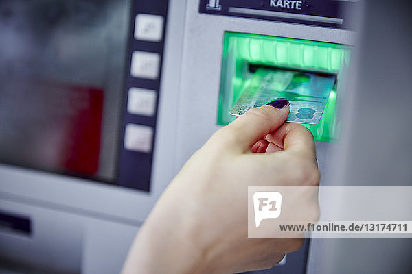 Nahaufnahme einer Frau  die eine Karte in den Schlitz eines Geldautomaten steckt