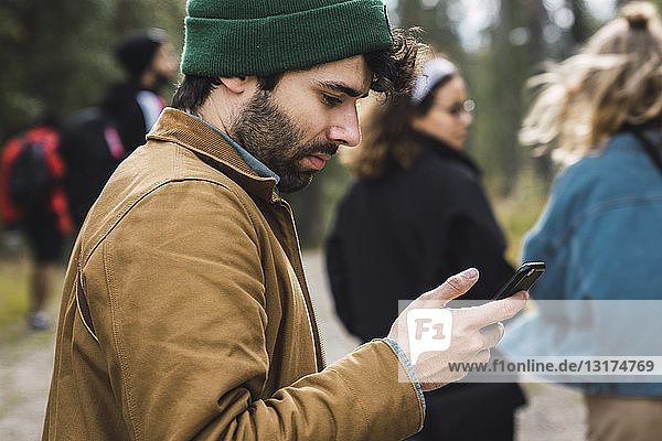 Man checking cell phone outdoors with friends in background