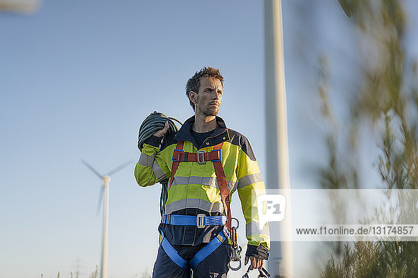 Techniker  der mit Kletterausrüstung an einem Windpark steht