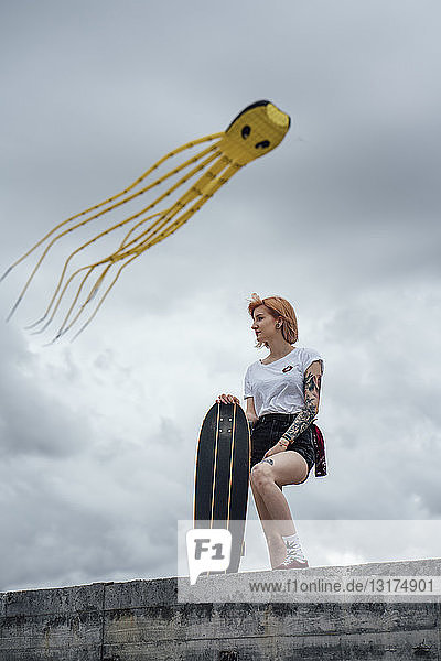 Junge Frau steht auf einer Betonwand auf einem Carver-Skateboard mit Drachen im Hintergrund