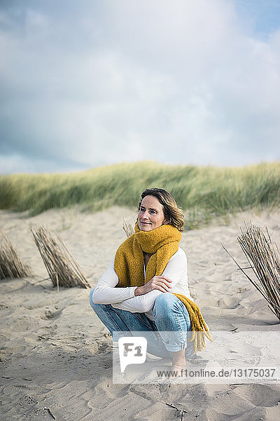 Reife Frau kauert in den Dünen und genießt den Wind