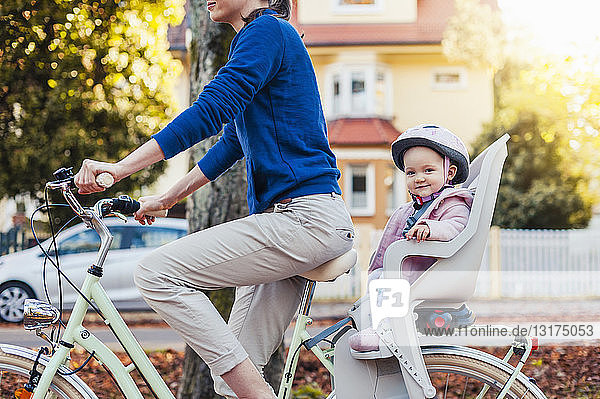 Mother and daughter riding bicycle  baby wearing helmet sitting in children's seat