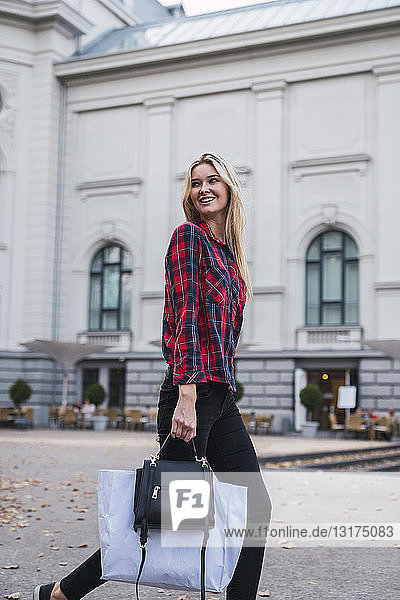 Portrait of smiling young woman with hand bag and shopping bag walking along