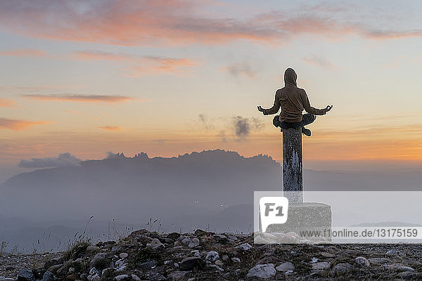 Spanien  Barcelona  Naturpark Sant Llorenc  Mann sitzt bei Sonnenuntergang in Yoga-Pose auf einer Stange