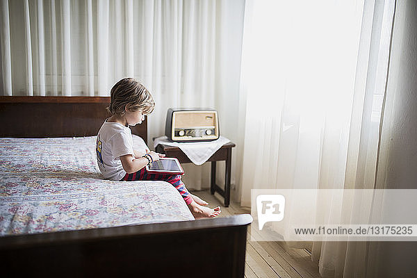 Young boy sitting on bed using a tablet