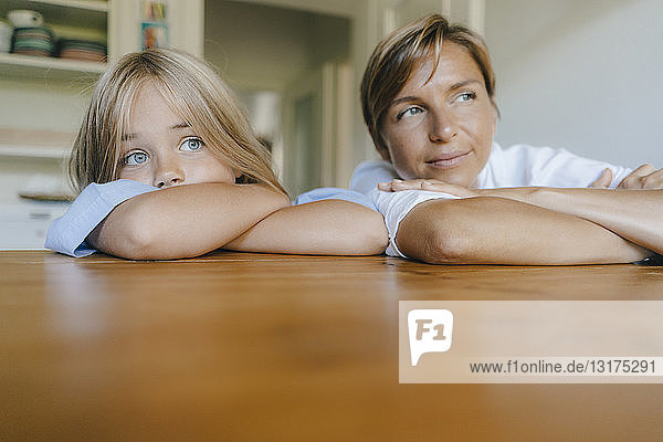 Mother and daughter leaning on kitchen table at home
