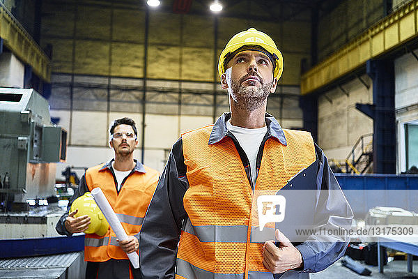 Zwei Männer in Arbeitsschutzkleidung sehen sich in der Fabrik um